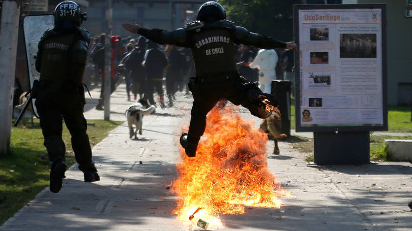 Um policial pula sobre uma bomba durante confrontos com estudantes que protestam por melhorias na educação do país e que aconteceu no Chile nesta semana. 