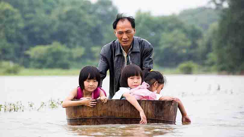 Um homem empurra uma banheira ofurô com crianças na volta para casa depois da escola em uma área inundada na província de Jiangxi.
